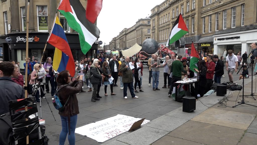 A rally of dozens of individuals in the middle of Newcastle's Monument area. Many of the attendees are holding either Palestinian flags or signs with Shireen Abu Akleh's image. 